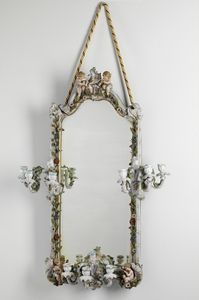 MANIFATTURA STADT, MEISSEN, XIX SECOLO - Specchio in porcellana riccamente decorato a motivi floreali, sormontato da due putti, nella parte inferiore putti musicanti, ai lati e nella parte inferiore candelabri a tre luci.