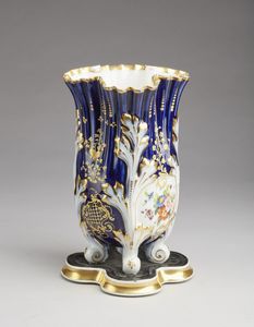 MANIFATTURA DEL XIX SECOLO - Vaso smaltato in porcellana parzialmente dorata e dipinta nei toni del blu e a decori floreali, poggiante su quattro piedini.