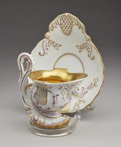 MANIFATTURA DI DRESDA DEL XIX-XX SECOLO - Tazzina in forma di elmo con piattino in porcellana dipinta e parzialmente dorata.